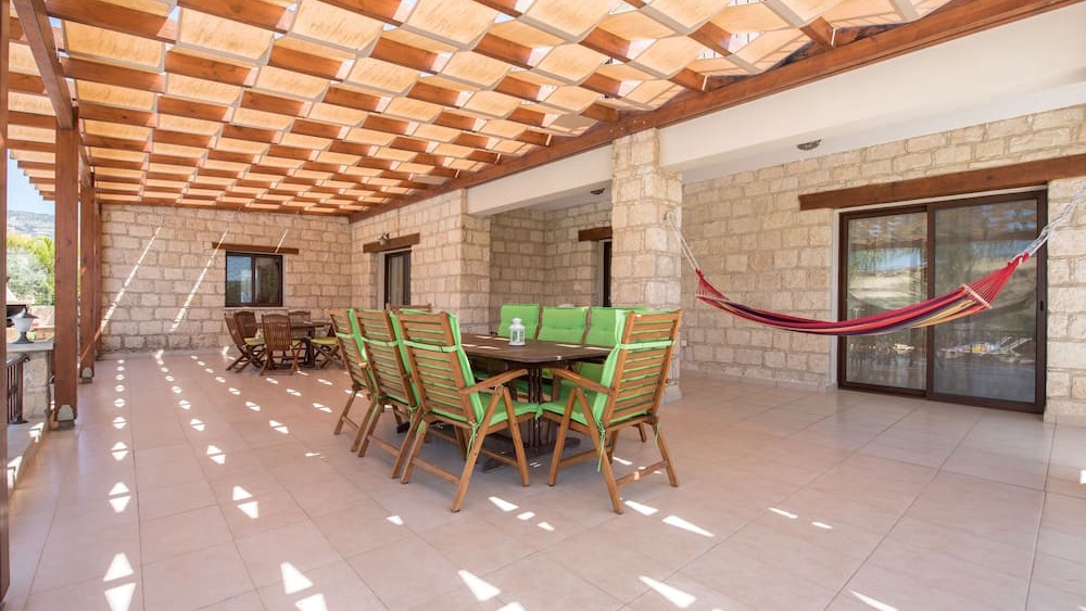 The covered terrace with a long dining table and a hammock, framed by stone walls